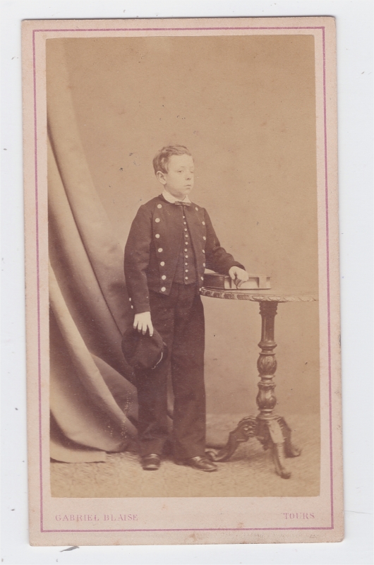 Collégien en uniforme, une main posée sur un album de photographies