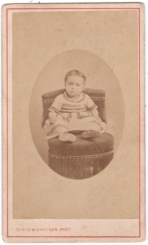 Bambin  en robe assis sur un fauteuil