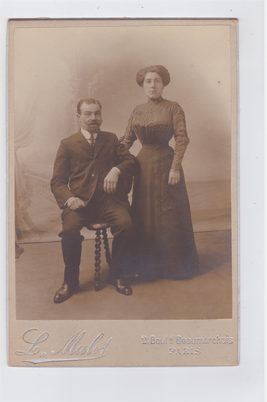 Couple : elle debout ; lui assis sur un tabouret